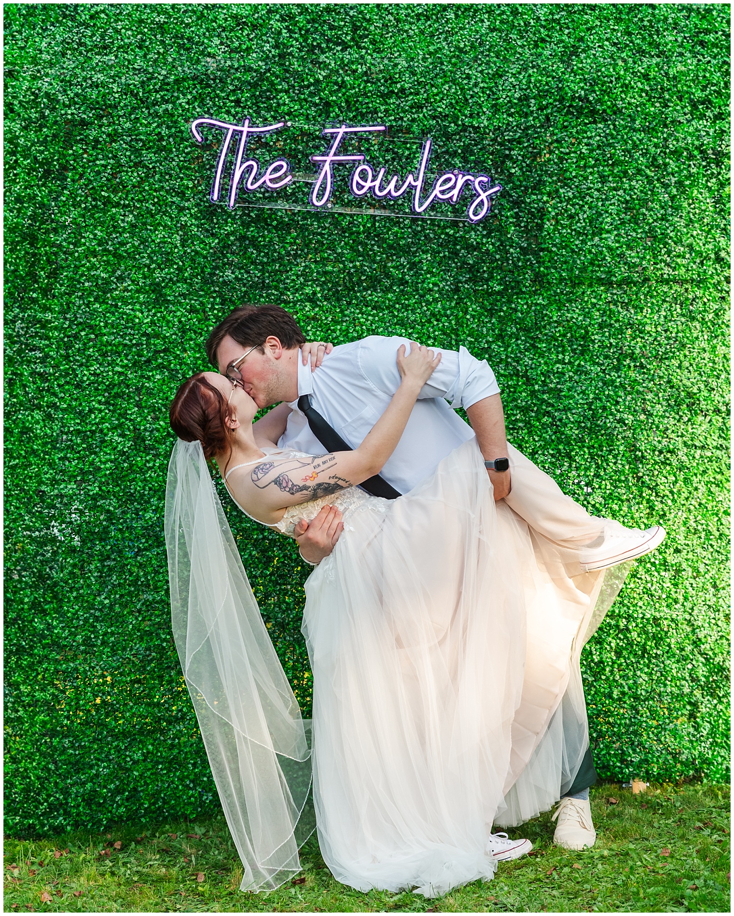 bride and groom kiss in front of greenery wall at wedding in baraga mi