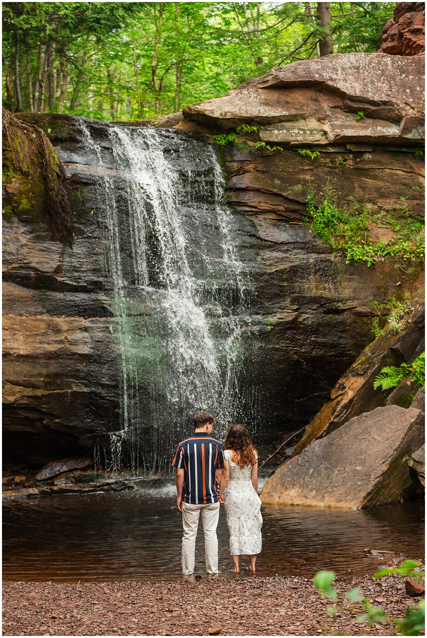 couple stands at base of hungarian falls waterfall before proposal in keweenaw peninsula upper peninsula