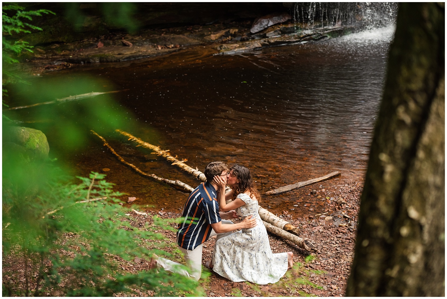 couple share tender moment after surprise proposal in front of waterfall in the upper peninsula of michigan